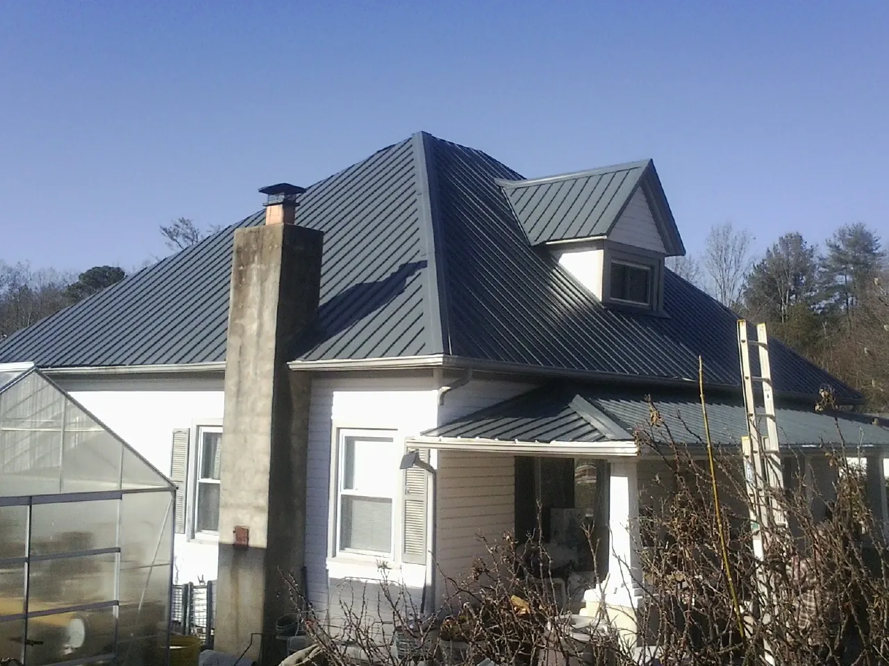 Dark blue standing seam metal roof on a white farmhouse with dormer — Slate & Tile Roof Repair by Roofing Brothers in Merlin