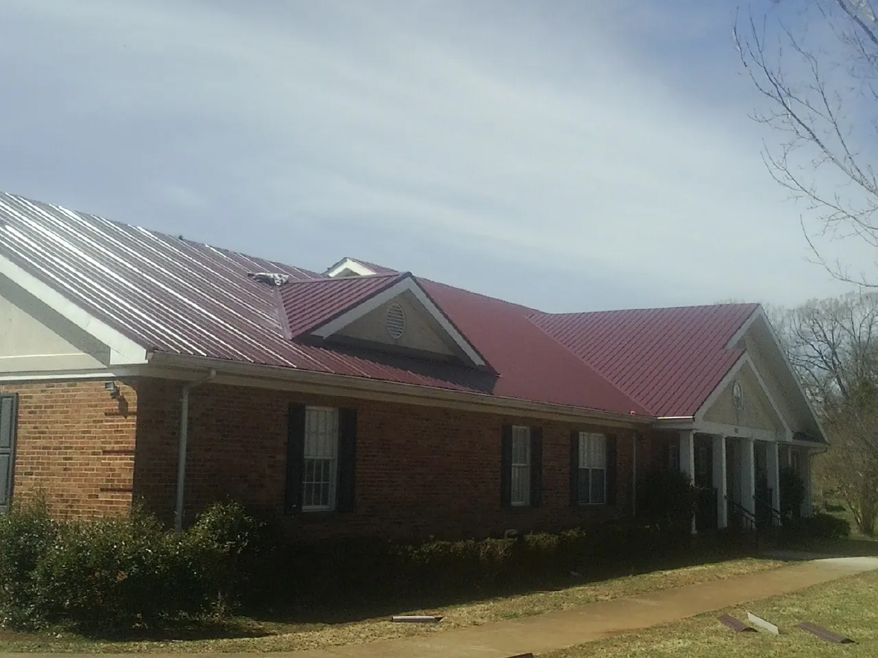 Red metal roof with gabled entries on a long brick building, from a Hail Damage Roof Repair job in Merlin