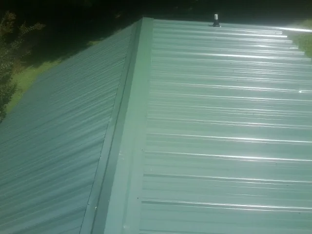 New green metal panels meeting at the ridge of a roof — Flat Roof Repair work by our crew in Merlin