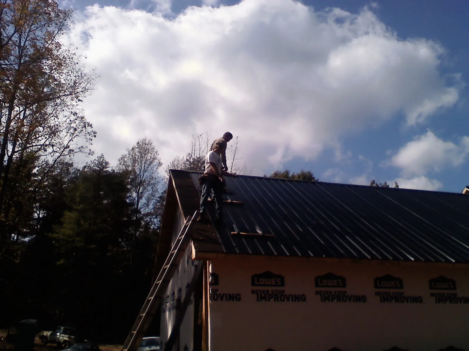 Roofer fastening dark metal panels high against a cloudy sky, from a Roof Inspection job in Merlin