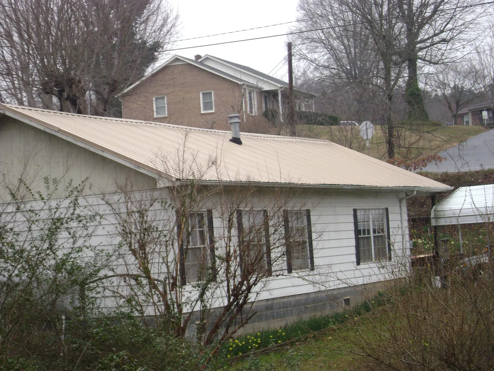 Tan metal roof on a white sided house set into a hillside — Commercial Roofing by Roofing Brothers in Merlin