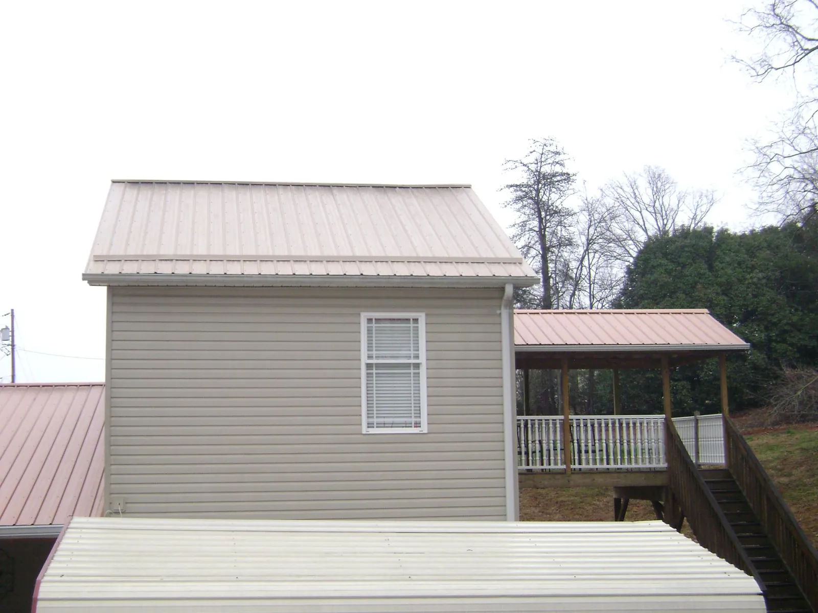 Tan metal roofs on a two story addition and attached porch, from a Roof Replacement job in Merlin