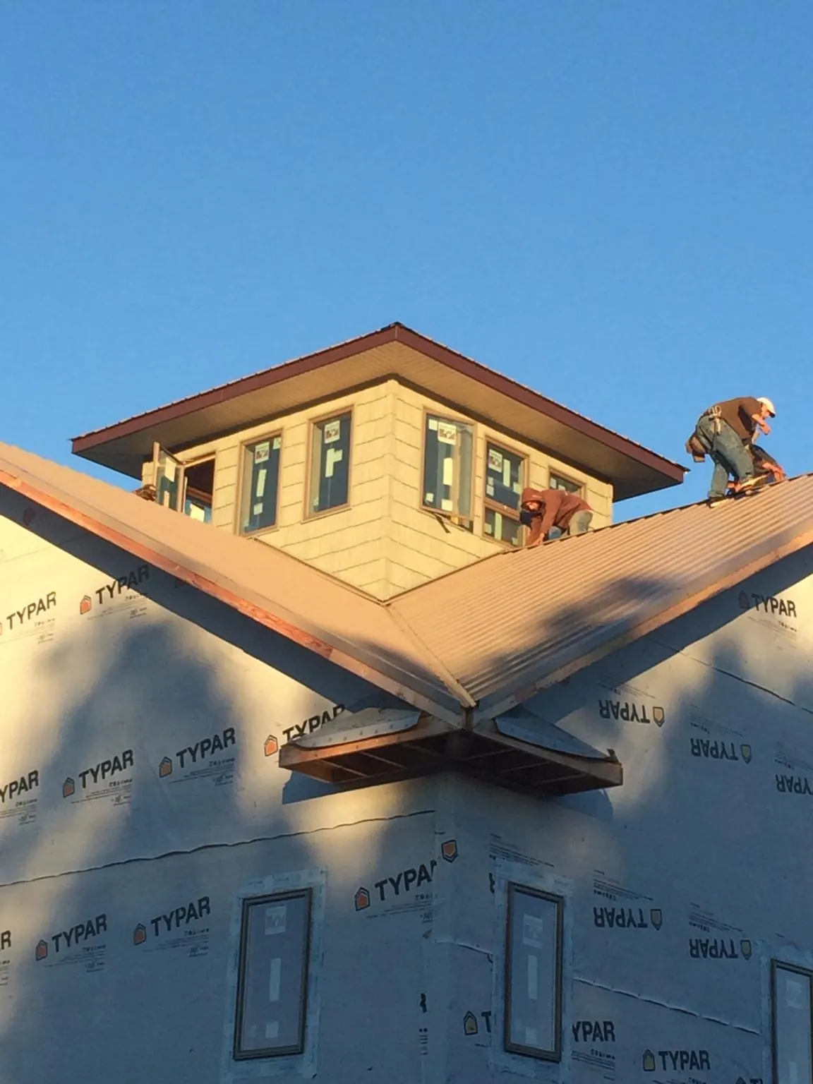 Roofers working around a rooftop cupola on a new metal roof at sunset in Merlin